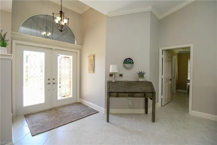 Foyer with french doors, a notable chandelier, a towering ceiling, and crown molding
