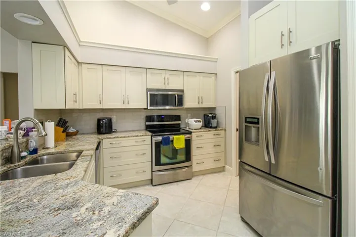 Kitchen with light tile patterned flooring, a sink, decorative backsplash, ornamental molding, and stainless steel appliances
