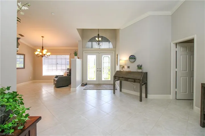 Entryway featuring light tile patterned floors, baseboards, an inviting chandelier, and crown molding
