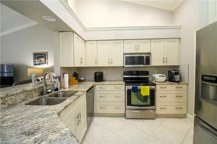 Kitchen with a sink, light stone counters, appliances with stainless steel finishes, crown molding, and light tile patterned floors