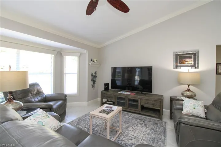 Tiled living room featuring vaulted ceiling, ornamental molding, baseboards, and ceiling fan