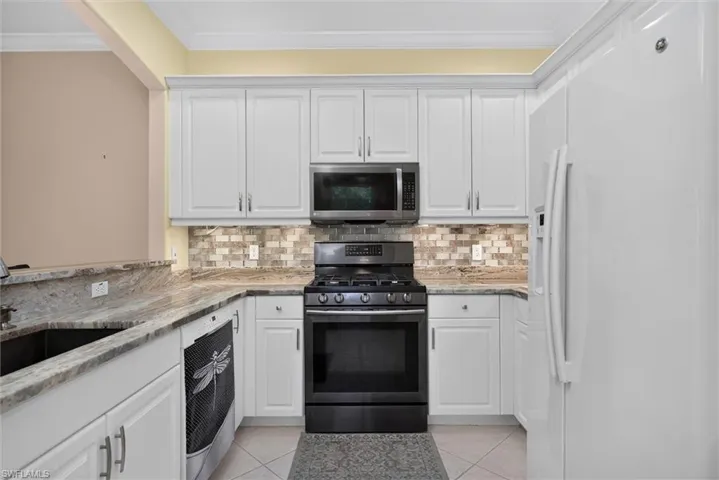 Kitchen featuring white cabinetry, stone countertops, stainless steel appliances, mosaic tile backsplash, and light-toned floor tiling