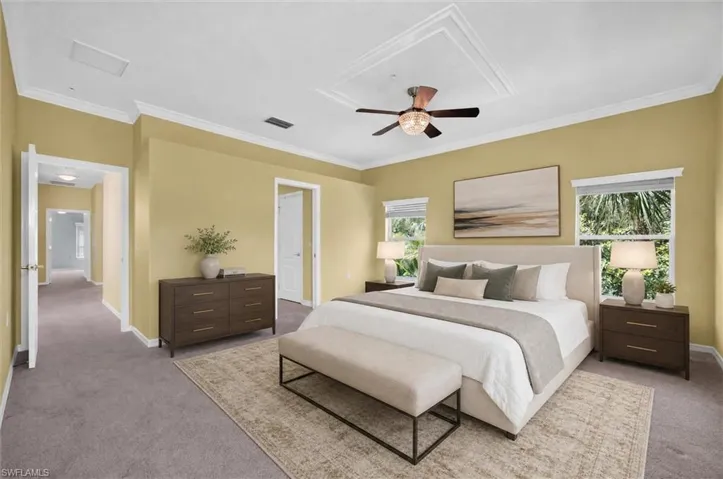 Spacious bedroom featuring crown molding, a tray ceiling with a modern ceiling fan, and multiple windows providing ambient light