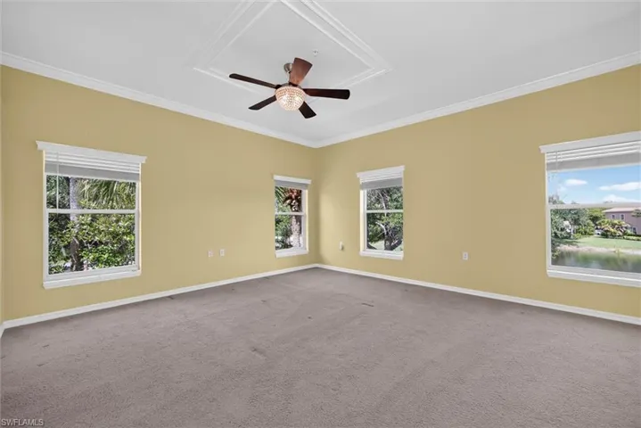 Spacious room featuring a tray ceiling with a central fan light fixture, crown molding, and neutral-toned carpeting