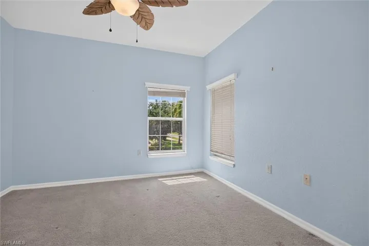 Carpeted interior space with vaulted ceilings, a ceiling fan with leaf-shaped blades, and two windows providing natural light