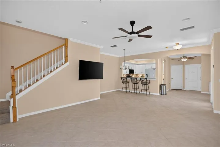 Spacious open-concept living area featuring large format tile flooring, crown molding, and a staircase with wood newel post and balusters
