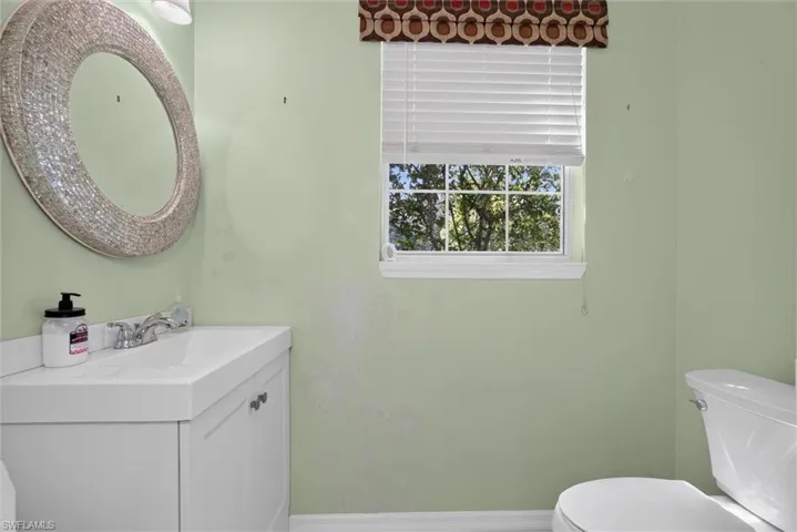 Bathroom featuring a white vanity with integrated sink, chrome faucet, and a round mosaic-tiled mirror