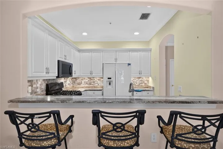 Kitchen featuring a breakfast bar with stone-finish countertop, white cabinetry, integrated microwave, and a mosaic tile backsplash