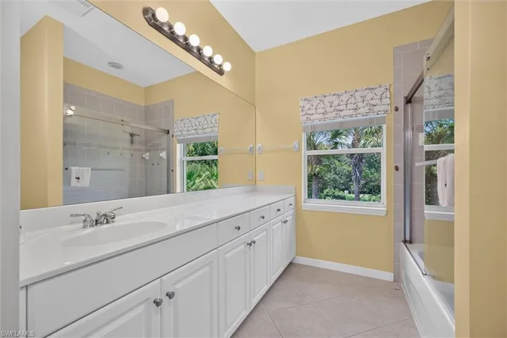 Bathroom vanity featuring a long countertop with an integrated sink, white cabinetry with silver hardware, and a full-width mirror