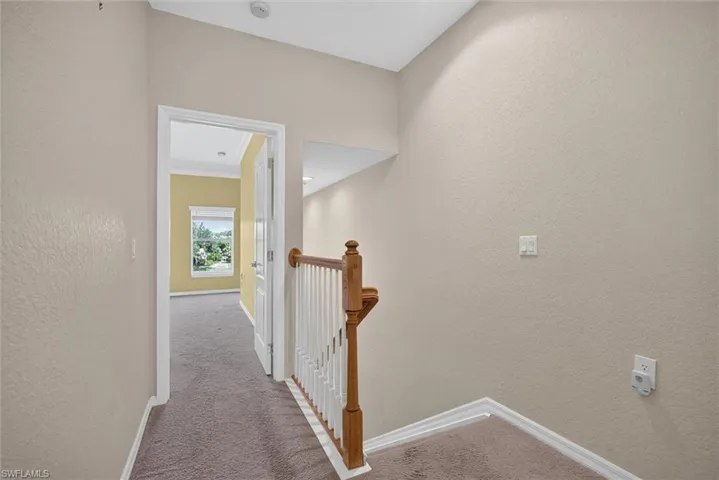 Carpeted hallway with light tan wall finishes, white trim, and a wood and white spindle staircase railing