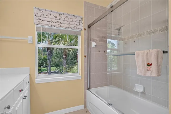 Bathroom featuring a tub/shower combination with sliding glass doors and light-colored wall tiles