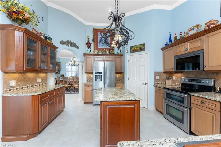 Kitchen featuring appliances with stainless steel finishes, backsplash, brown cabinets, a chandelier, and crown molding