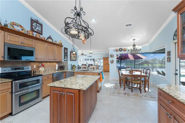 Kitchen with ornamental molding, appliances with stainless steel finishes, brown cabinets, a chandelier, and pendant lighting