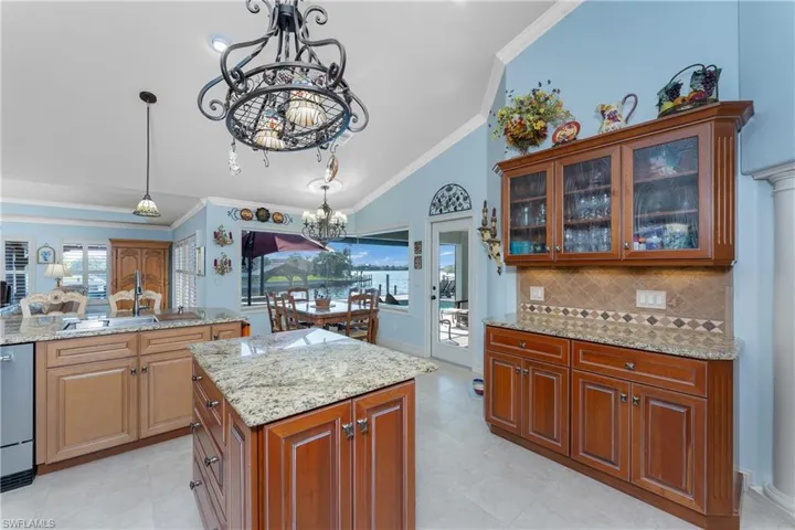 Kitchen with ornamental molding, pendant lighting, light stone countertops, a kitchen island, and a chandelier