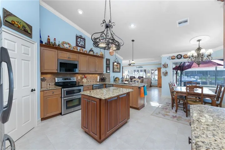 Kitchen featuring a chandelier, crown molding, a peninsula, brown cabinetry, and appliances with stainless steel finishes