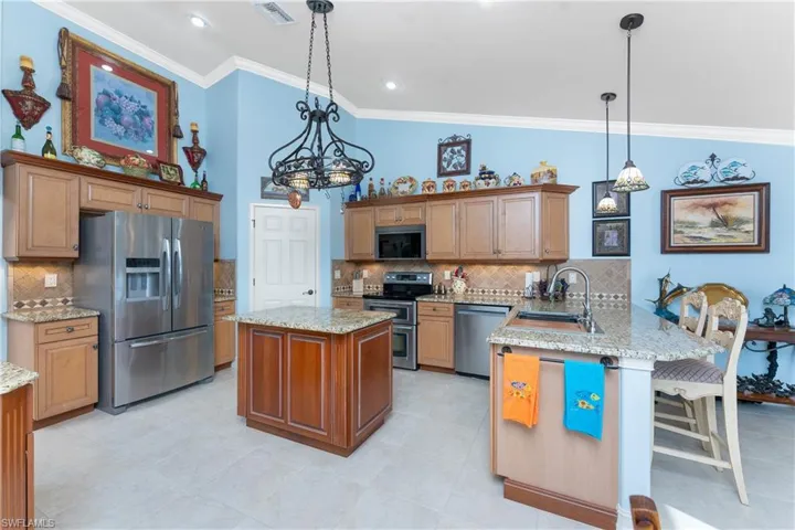 Kitchen with a peninsula, stainless steel appliances, brown cabinets, crown molding, and hanging light fixtures