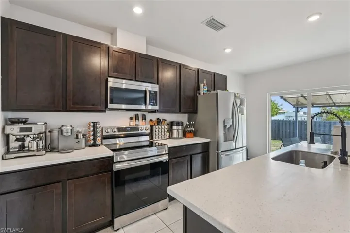 Kitchen with appliances with stainless steel finishes, dark brown cabinets, light stone countertops, light tile patterned floors, and recessed lighting