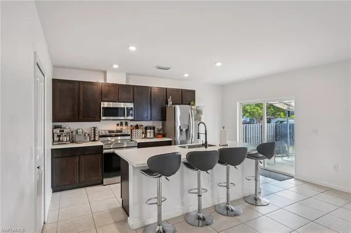 Kitchen with stainless steel appliances, a center island with sink, a breakfast bar area, dark brown cabinets, and light tile patterned floors