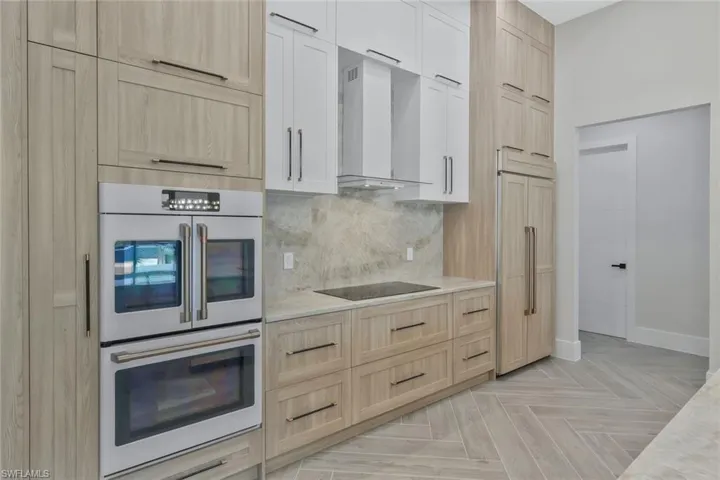 Kitchen featuring light brown cabinetry, white double oven, paneled refrigerator, wall chimney range hood, and backsplash