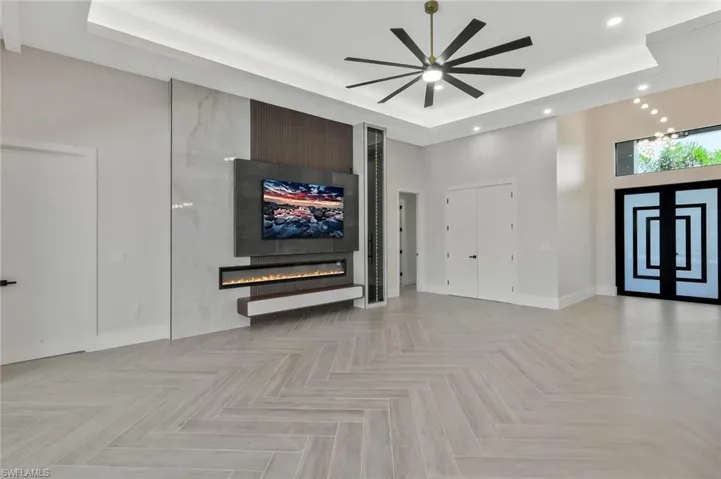 Unfurnished living room featuring a raised ceiling, a large fireplace, a towering ceiling, recessed lighting, and ceiling fan