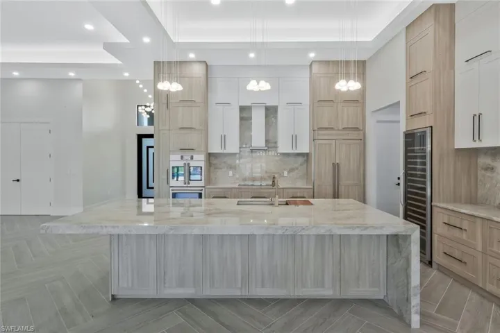 Kitchen featuring light stone countertops, light brown cabinetry, beverage cooler, a large island, and recessed lighting