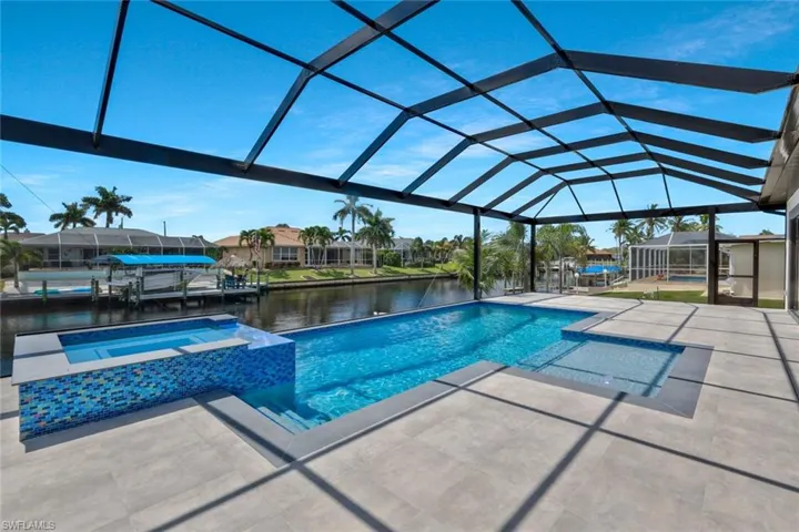 View of pool featuring a sunroom, a pool with connected hot tub, a water view, and glass enclosure