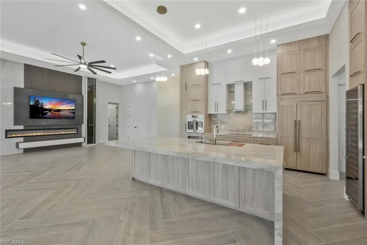 Kitchen with light brown cabinets, a tray ceiling, light stone countertops, open floor plan, and recessed lighting