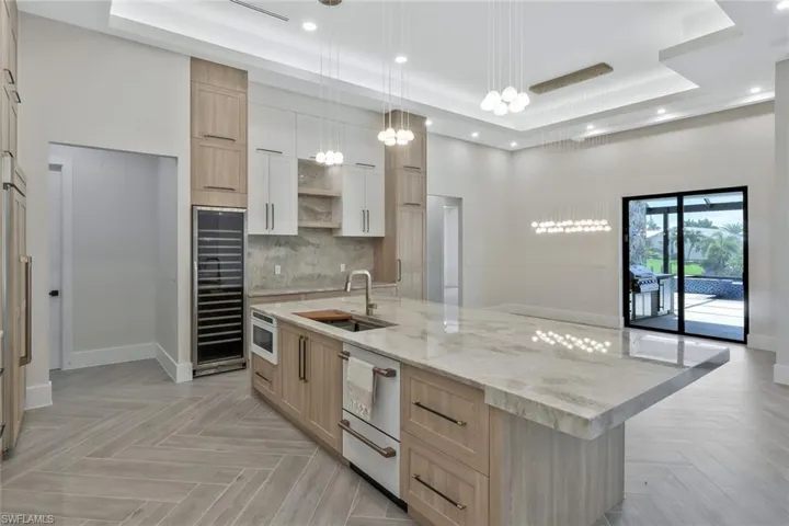 Kitchen with light brown cabinetry, a raised ceiling, tasteful backsplash, beverage cooler, and recessed lighting