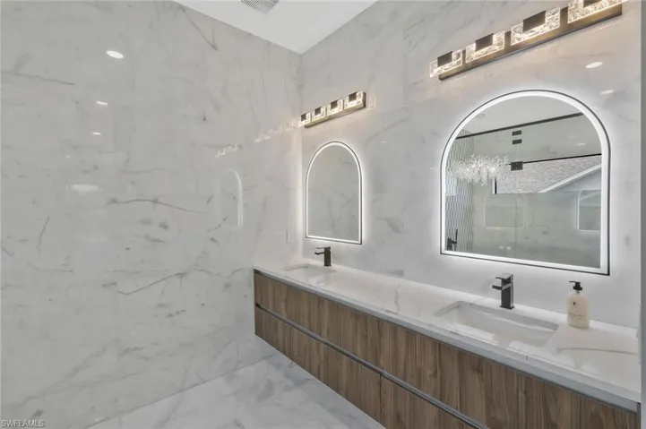 Bathroom with double vanity, tile walls, light marble finish flooring, stone wall, and a marble finish shower