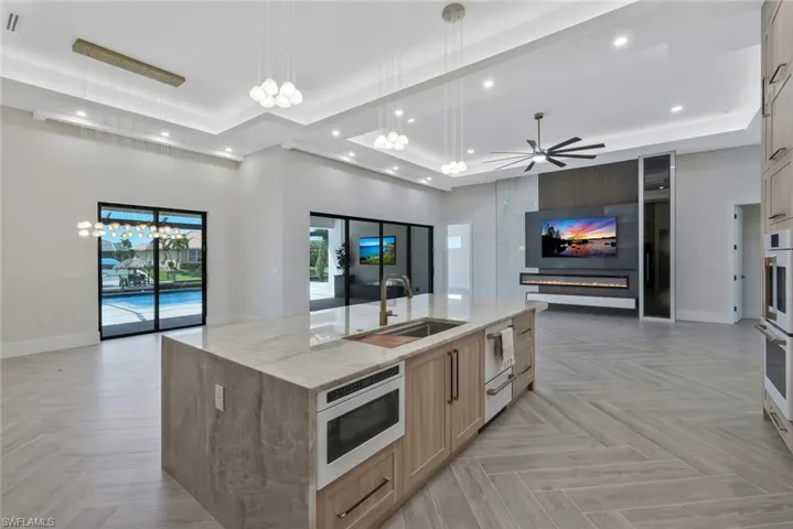 Kitchen featuring a tray ceiling, open floor plan, light stone countertops, light brown cabinetry, and a chandelier