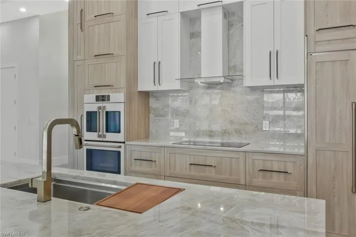 Kitchen featuring light brown cabinetry, wall chimney range hood, white double oven, and light stone countertops