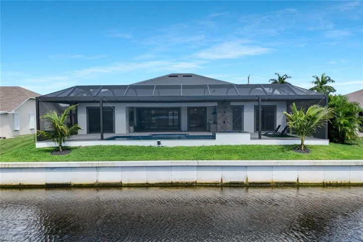Rear view of house with a sunroom, glass enclosure, a yard, and a water view