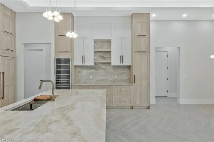 Kitchen featuring light brown cabinets, decorative light fixtures, backsplash, wine cooler, and recessed lighting