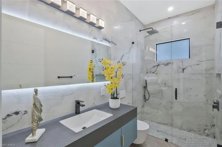 Bathroom featuring a marble finish shower, tile walls, and vanity