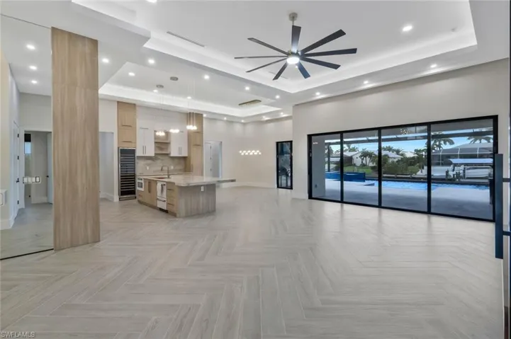 Kitchen featuring a tray ceiling, open floor plan, light brown cabinetry, backsplash, and a large island with sink