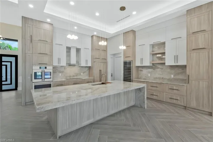 Kitchen featuring light brown cabinets, light stone countertops, open shelves, hanging light fixtures, and beverage cooler