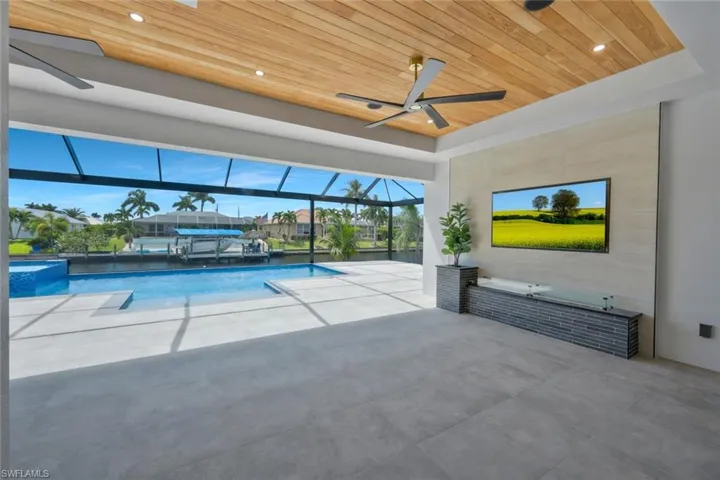 View of patio featuring glass enclosure, ceiling fan, and a pool with connected hot tub