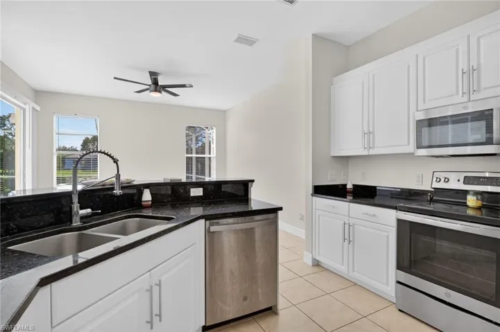 Kitchen with stainless steel appliances, white cabinetry, dark stone counters, light tile