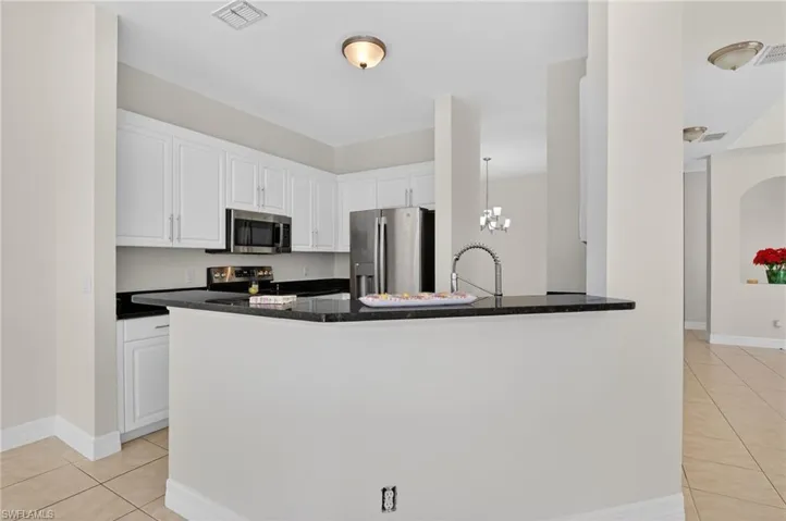 Kitchen with white cabinets, light tile patterned floors, stainless steel appliances, decorative light fixtures, and a peninsula