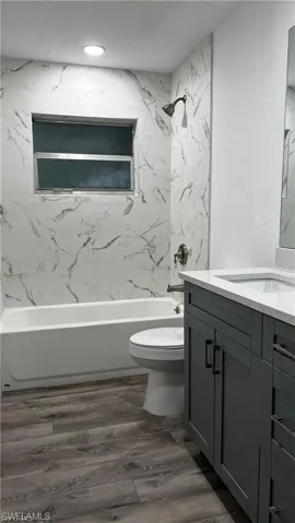Bathroom with toilet, vanity, bathtub / shower combination, and wood finished floors
