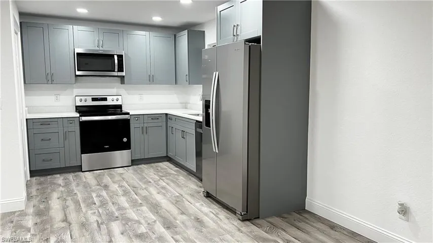 Kitchen with light countertops, stainless steel appliances, baseboards, gray cabinetry, and light wood-style flooring