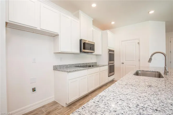 Kitchen with light stone counters, wood tiled floors, white cabinetry, and recessed lighting