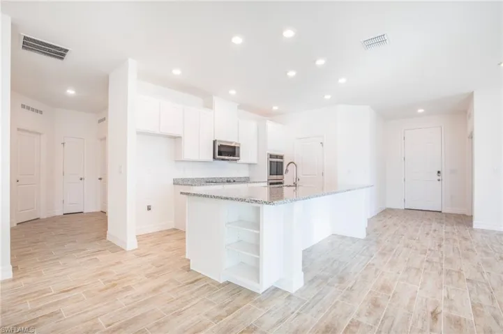 Kitchen featuring white cabinets, open shelves, wood tiled floors, a center island with sink, and light stone counters