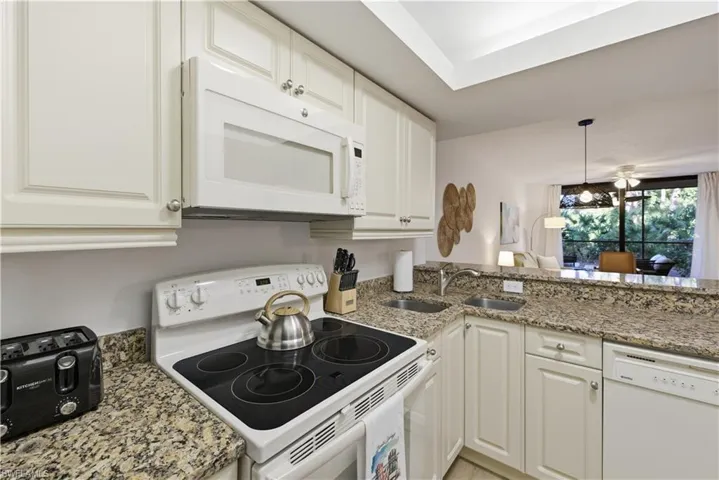 Kitchen with white appliances, light stone counters, pendant lighting, and white cabinets
