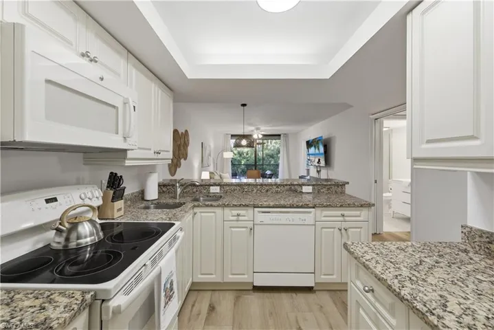 Kitchen with white appliances, light stone countertops, white cabinetry, light wood-style floors, and a peninsula