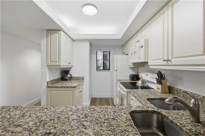Kitchen featuring white appliances, light stone countertops, light wood finished floors, and white cabinetry