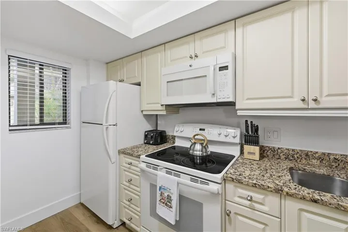 Kitchen featuring white appliances, light stone counters, light wood finished floors, and cream cabinetry