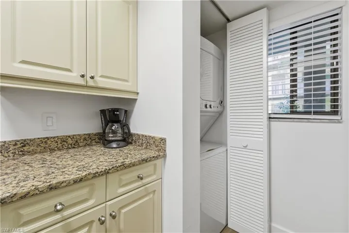 Bar area with light stone counters, stacked washer / drying machine, and cream cabinets