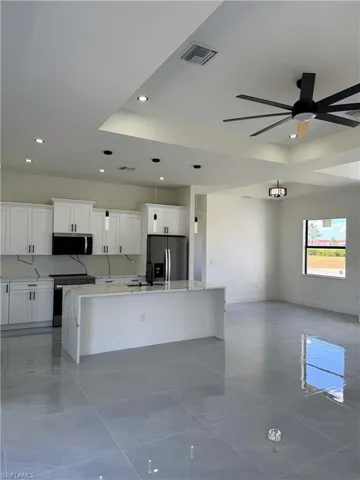 Kitchen featuring light stone counters, stainless steel appliances, a center island with sink, white cabinetry, and a tray ceiling