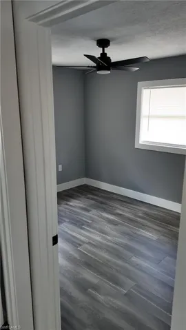 Unfurnished room with ceiling fan, dark wood-style floors, and a textured ceiling